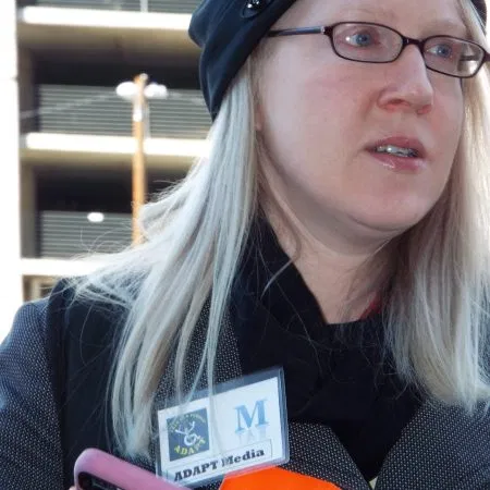 Picture of Kathryn Carroll Picture of a woman with blonde hair, wearing a black cap, eye glasses, a black scar and dark coat.