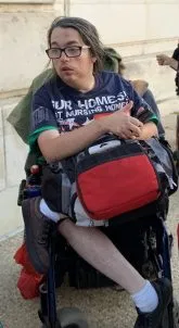 Picture of Jordan Sibayan Picture of a person in a power wheelchair holding a red and black bag.