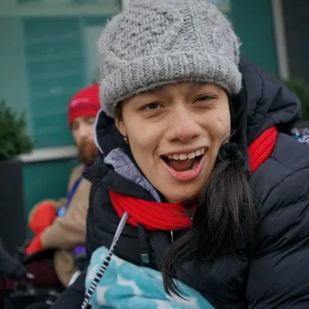Picture of a person with a grey winter hat, dark coat with red scar.