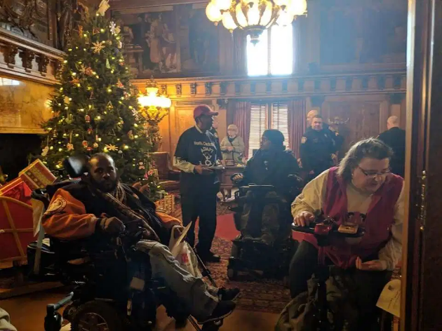 A group of people, some in wheelchairs and some standing in a room with a decorated Christmas tree.