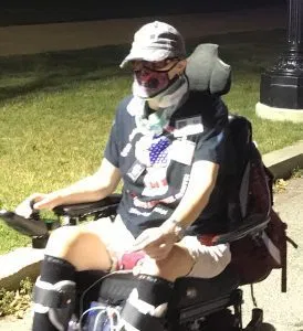 Picture of Kimberly Jackson Person in a power wheelchair with a cap and mask, dark shirt and shorts.