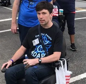 Picture of Liam Dougherty A person in a power wheelchair wearing an ADAPT tee shirt and dark pants.