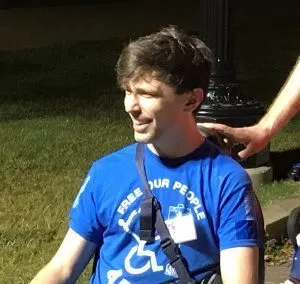 Picture of Liam Dougherty A man with short brown hair and a blue top that says "Free Our People" smiles as he looks into the distance.
