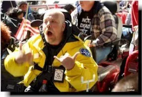 A man in a wheelchair wearing a yellow coat and ADAPT nametag