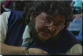 A man with dark curly hair and glasses looks off to the right at something off camera.