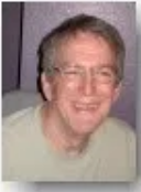 A man with glasses and a light top looks into the camera.