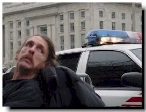 A man in a wheelchair sits in front of a police car.