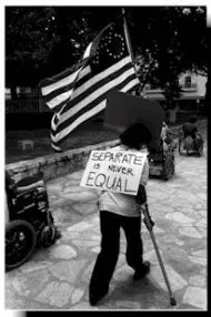Black and white image of an ADAPT protestor walking with crutches. A sign is on their back that says "Separate is never Equal." An American flag has the stars in the shape of a wheelchair.