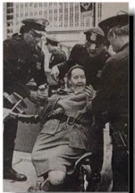 Black and white photo of a person in a wheelchair surrounded by police officers.