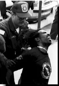 ADAPT protester being arrested Black and white picture of a male ADAPT protestor being arrested by police. He is kneeling on the ground with his mouth opened in a shout or yell.