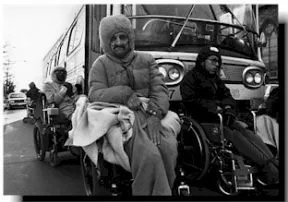 Black and white photo of people in wheelchairs and winter coats surrounding a city bus.