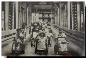 Black and white photo of a group of people in wheelchairs rolling down a bridge.