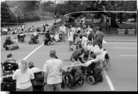 Black and white picture of a group of people, standing and in wheelchairs, forming a circle at an intersection.