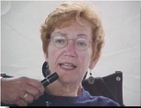 A woman with short red hair and glasses speaks into a microphone