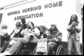 Picture of ADAPT protestors in front of the Georgia Nursing Home Association Black and white picture of ADAPT protestors, some in wheelchairs and some standing, in front of a building sign for Georgia Nursing Home Association