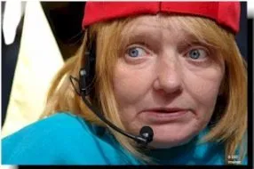 A person with blonde hair, red cap, blue top, and a microphone headset looks at something off camera.