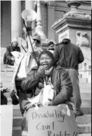 A black and white photo of a person sitting in front of a flight of outdoor stairs holding a sign "Disability Civil Rights"