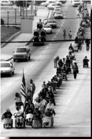 Black and white picture of people walking and in wheelchairs marching in the street in protest.