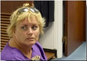 A woman with short blonde hair and a purple top looks off into the distance.