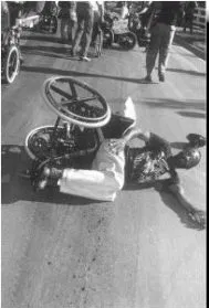 Black and white photo of a person in an overturned wheelchair in the middle of the street.