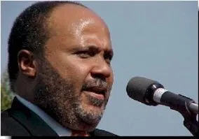 A Black man with a beard and mustache, wearing a dark suit speaks into a microphone. Martin Luther King III