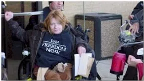 Picture of Cassie James A woman with short red hair and a dark top that says "Freedom Now" looks towards the camera.