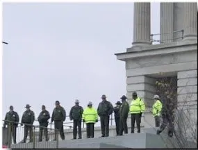 Police officers and Troopers line up side-by-side in front of a large building.