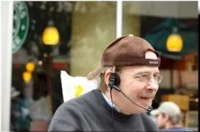 Picture of Steve Verriden A man with a backwards brown cap, glasses, and a dark top speaks into a microphone headset.